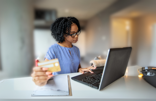 A therapist in a clinic setting reviews payment tracking and billing reconciliation data on a computer while holding a credit card, symbolizing financial management in healthcare